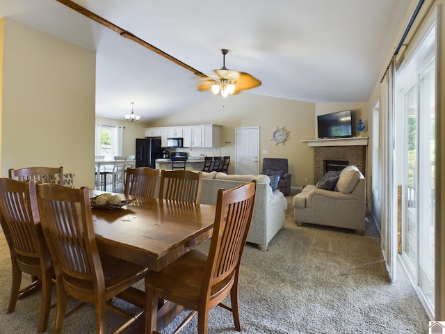 dining area with carpet, ceiling fan with notable chandelier, a fireplace, and lofted ceiling