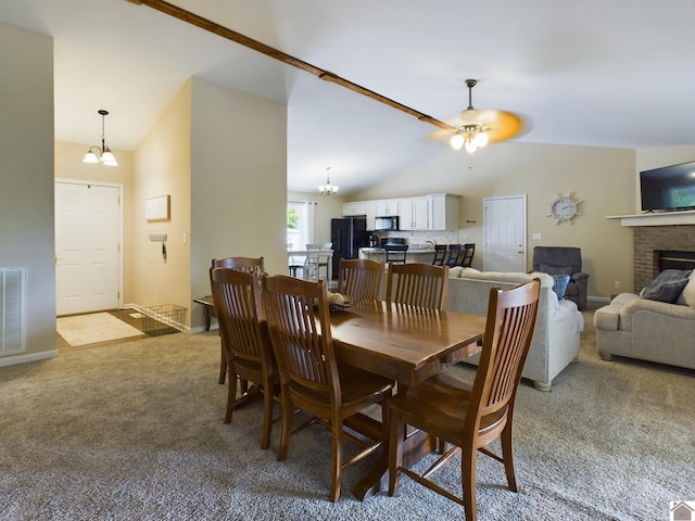 carpeted dining space featuring high vaulted ceiling, a fireplace, and ceiling fan with notable chandelier