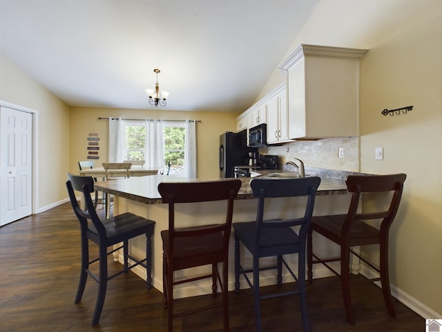 kitchen with dark hardwood / wood-style floors, a kitchen breakfast bar, black appliances, lofted ceiling, and a chandelier