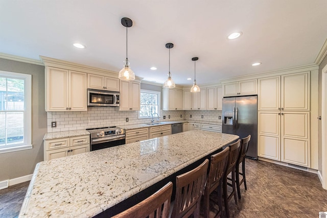 kitchen featuring light stone counters, crown molding, decorative light fixtures, cream cabinetry, and appliances with stainless steel finishes