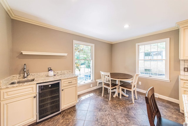 kitchen featuring light stone counters, beverage cooler, crown molding, sink, and cream cabinetry