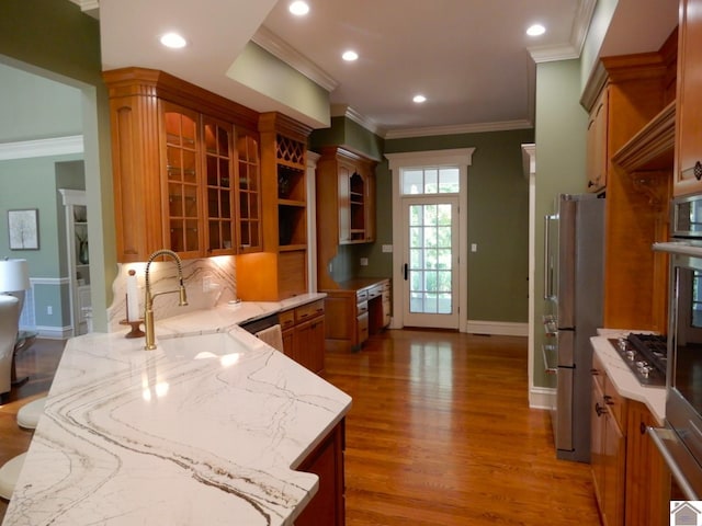 kitchen featuring hardwood / wood-style flooring, stainless steel appliances, crown molding, light stone counters, and sink