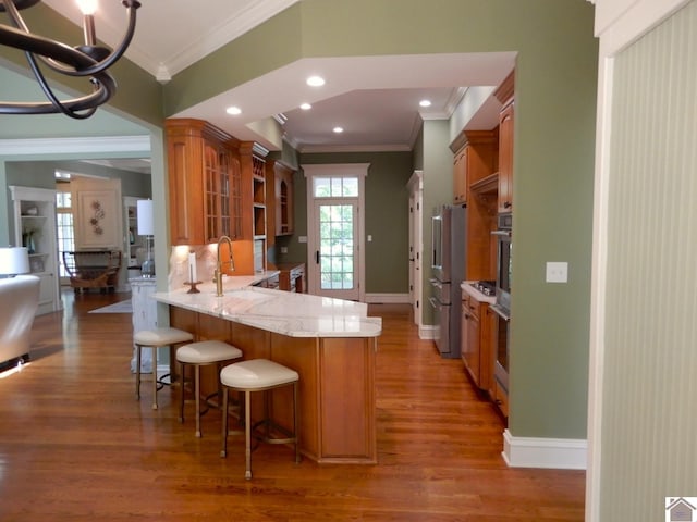 kitchen featuring a breakfast bar, kitchen peninsula, sink, stainless steel appliances, and ornamental molding