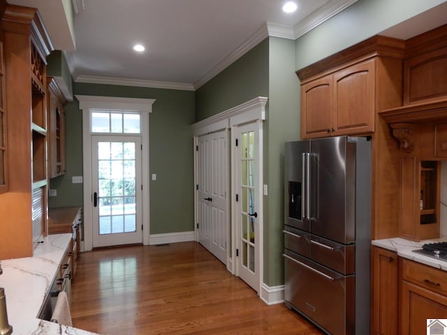 kitchen with black gas cooktop, high end refrigerator, crown molding, light wood-type flooring, and light stone counters