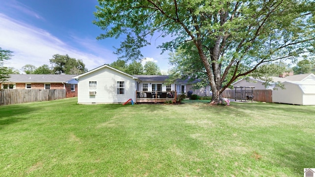 rear view of property with a lawn, a wooden deck, and a storage unit