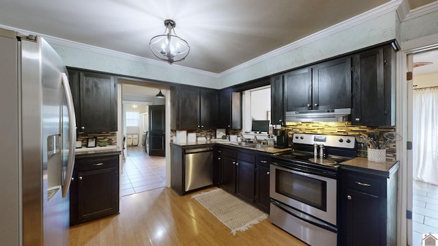 kitchen with crown molding, hanging light fixtures, appliances with stainless steel finishes, tasteful backsplash, and light hardwood / wood-style floors