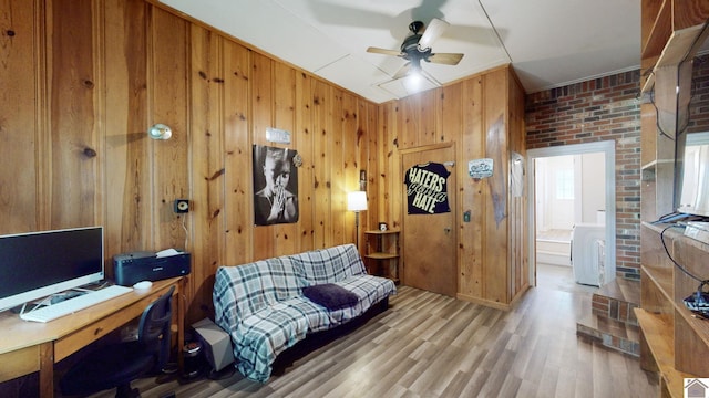 office area with ceiling fan, brick wall, wood walls, and light wood-type flooring