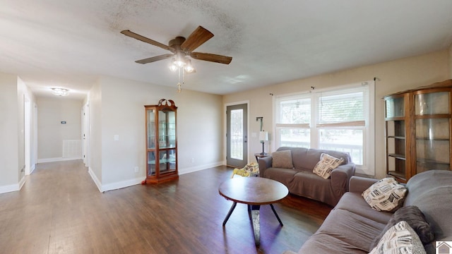 living room with a textured ceiling, ceiling fan, and dark wood-type flooring