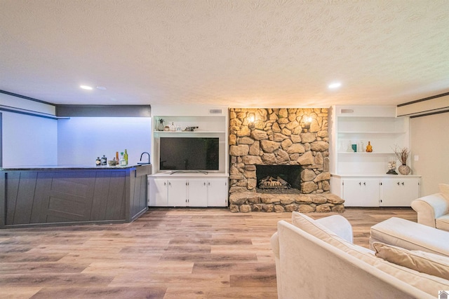 living room featuring a stone fireplace, built in shelves, a textured ceiling, and light wood-type flooring