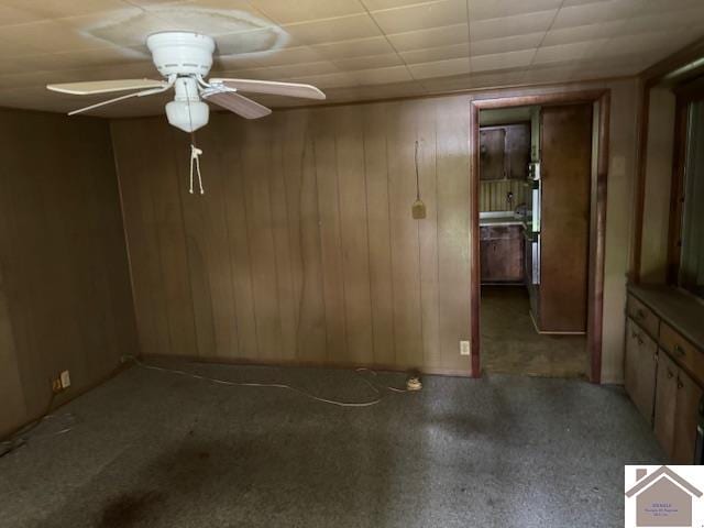 carpeted spare room with wood walls and ceiling fan