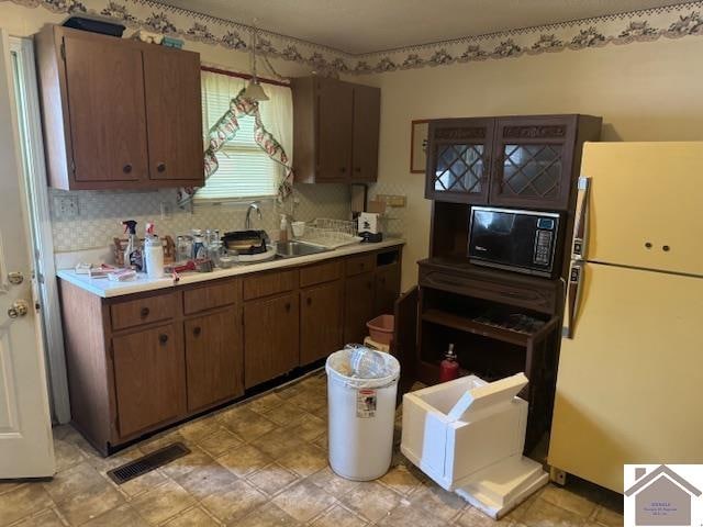 kitchen with dark brown cabinetry, sink, white fridge, and backsplash