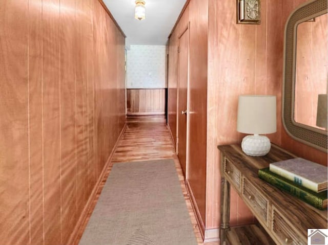 corridor with light wood-type flooring and wood walls