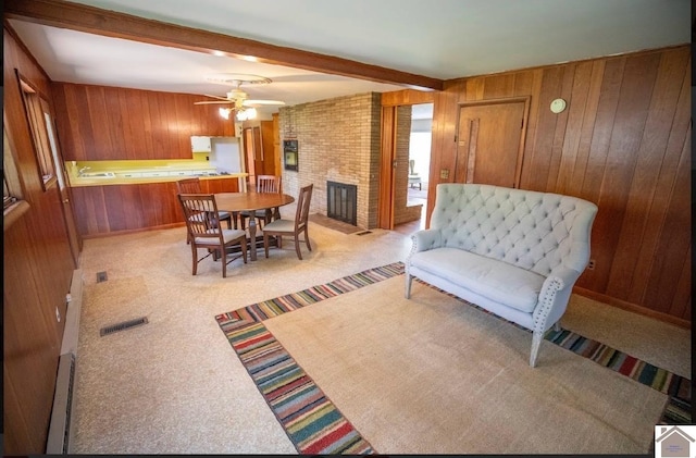 dining area featuring a fireplace, light colored carpet, wood walls, ceiling fan, and beam ceiling