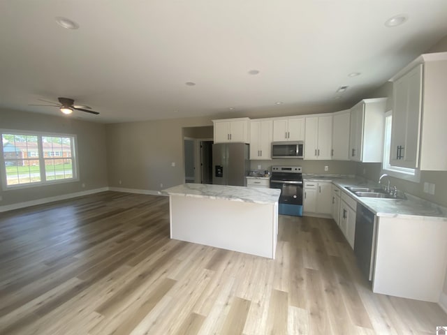 kitchen with a sink, white cabinetry, open floor plan, appliances with stainless steel finishes, and a center island