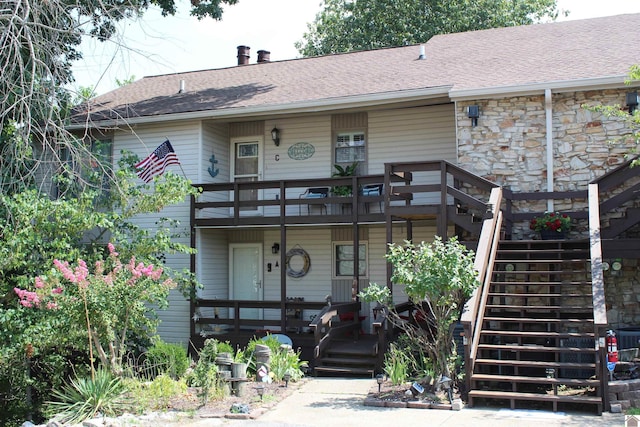 view of front of property with covered porch, a shingled roof, stone siding, and stairway