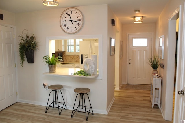 kitchen featuring tasteful backsplash, light wood-type flooring, white refrigerator with ice dispenser, and a breakfast bar