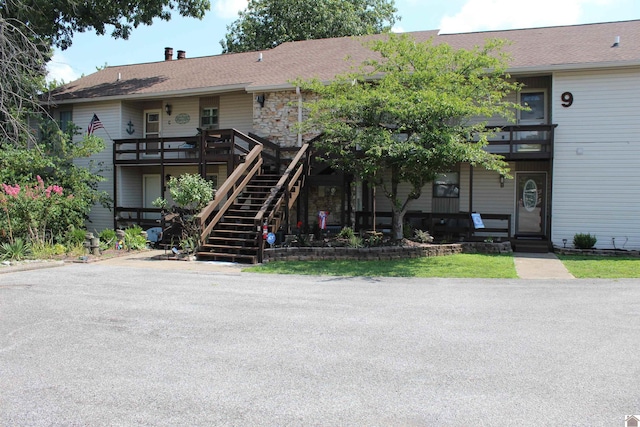 view of front of property with stone siding, stairway, and roof with shingles