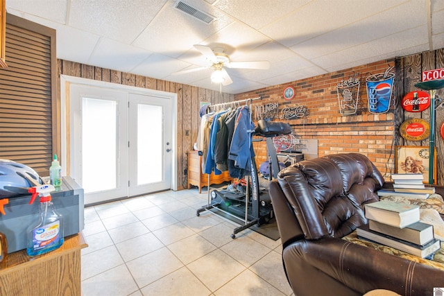 interior space with wood walls, a drop ceiling, ceiling fan, and french doors