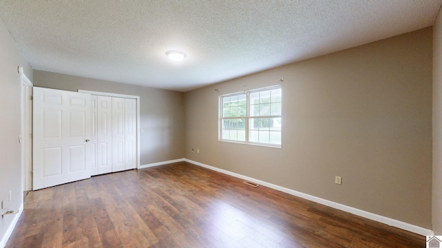 unfurnished bedroom featuring a textured ceiling, dark hardwood / wood-style flooring, and a closet