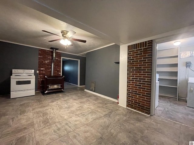 unfurnished living room with brick wall, a wood stove, a ceiling fan, washer / dryer, and crown molding