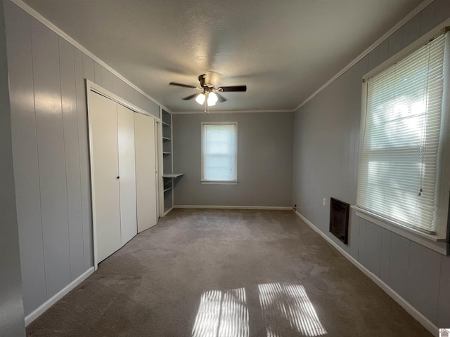 unfurnished bedroom with ceiling fan, ornamental molding, a closet, and carpet