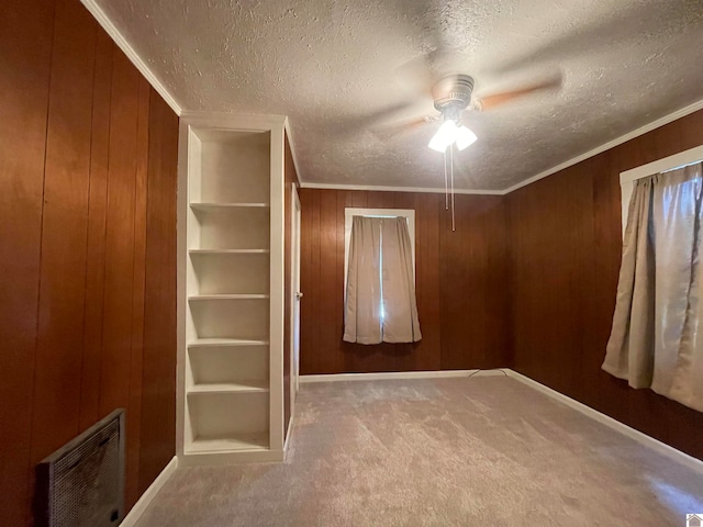 spare room with wooden walls, carpet floors, a textured ceiling, ceiling fan, and ornamental molding