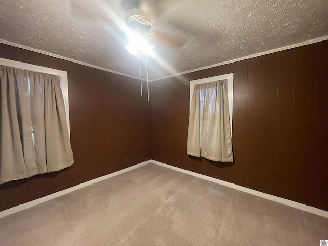 carpeted spare room featuring ornamental molding, ceiling fan, a textured ceiling, and baseboards