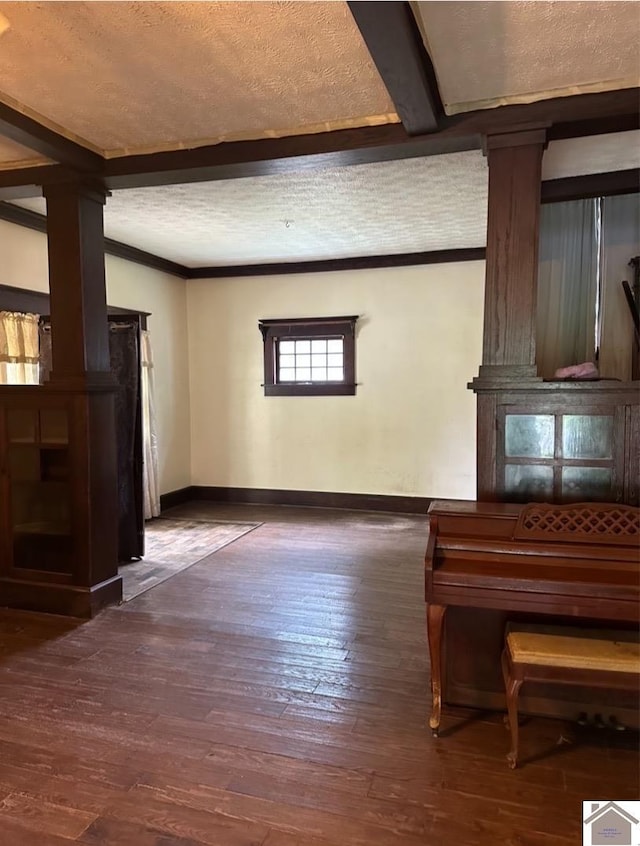 interior space featuring dark hardwood / wood-style floors, a textured ceiling, and ornate columns