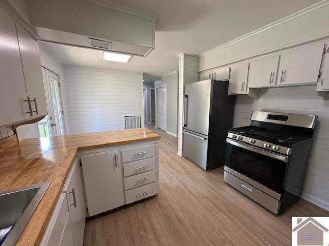 kitchen with appliances with stainless steel finishes, white cabinetry, butcher block counters, sink, and light wood-type flooring