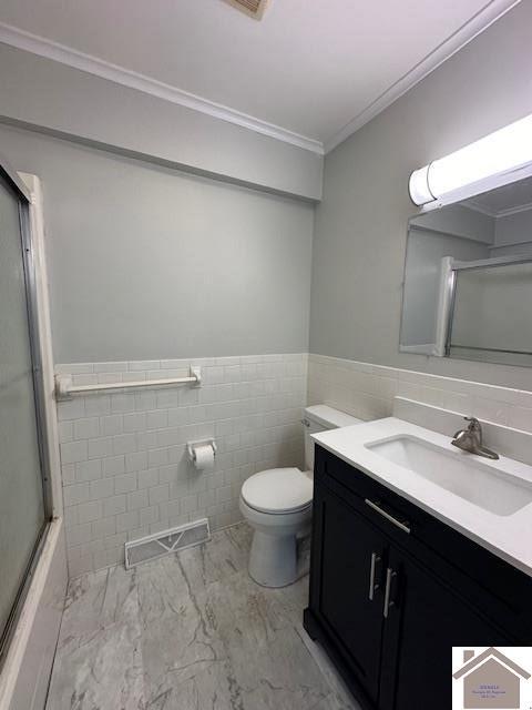 bathroom with a shower with door, tile walls, vanity, ornamental molding, and toilet