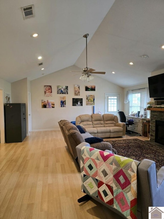 living room featuring light hardwood / wood-style floors, lofted ceiling, a stone fireplace, and ceiling fan