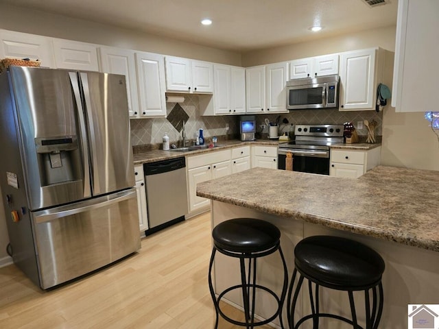 kitchen featuring a breakfast bar area, light hardwood / wood-style flooring, stainless steel appliances, decorative backsplash, and white cabinetry