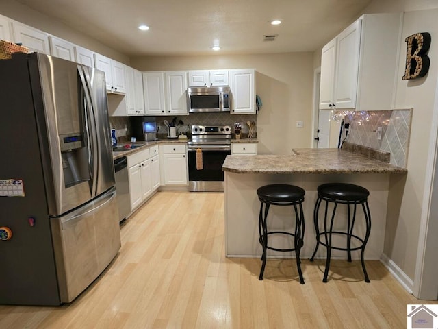 kitchen with white cabinetry, tasteful backsplash, stainless steel appliances, light hardwood / wood-style floors, and a kitchen bar