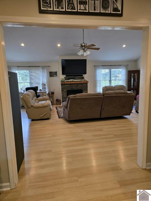 living room featuring a stone fireplace, ceiling fan, and light hardwood / wood-style flooring