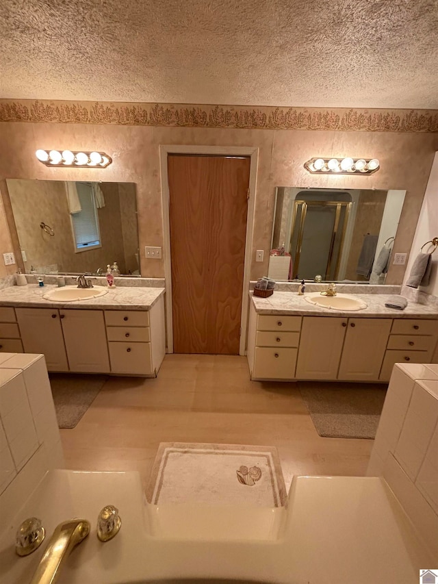 bathroom with double sink vanity, a bath, and a textured ceiling