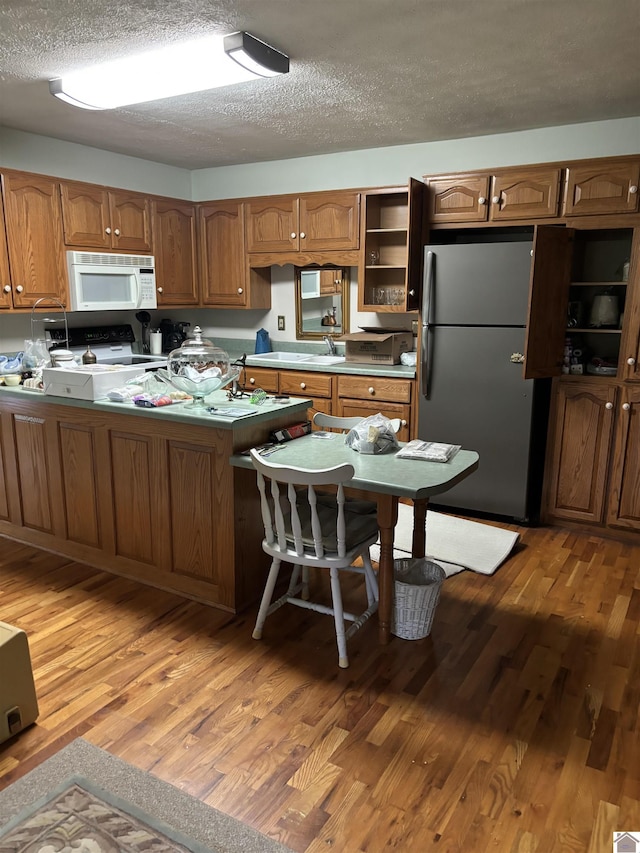 kitchen featuring sink, a textured ceiling, light wood-type flooring, stainless steel refrigerator, and range with electric cooktop