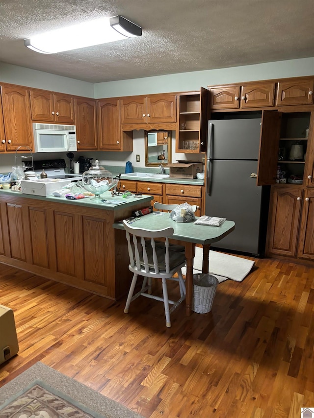 kitchen with sink, range with electric stovetop, stainless steel fridge, light hardwood / wood-style flooring, and a textured ceiling