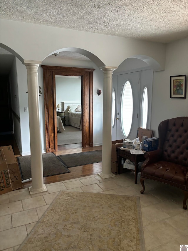 entrance foyer featuring a textured ceiling, decorative columns, and light tile patterned floors