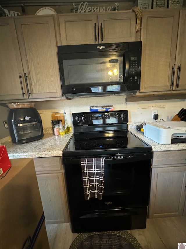 kitchen with black appliances, light stone countertops, and wood-type flooring