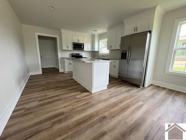 kitchen with sink, wood-type flooring, a kitchen island, white cabinetry, and stainless steel appliances