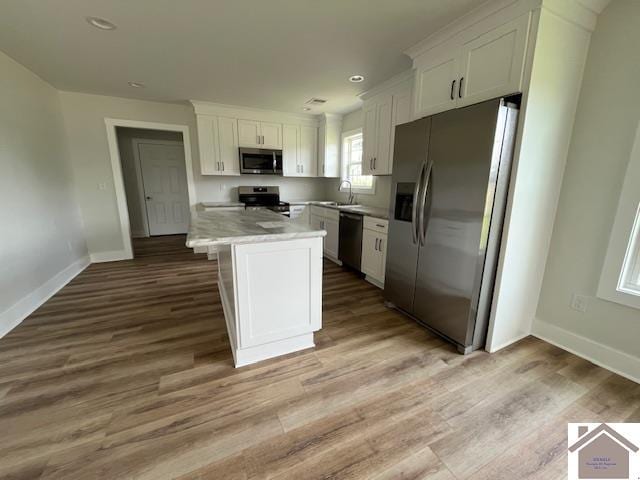 kitchen featuring appliances with stainless steel finishes, hardwood / wood-style floors, white cabinetry, sink, and a center island