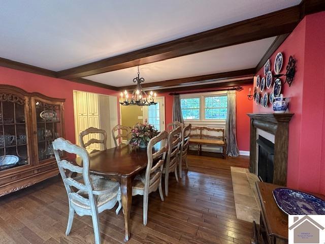 dining area featuring a chandelier, dark wood-type flooring, beamed ceiling, and a glass covered fireplace