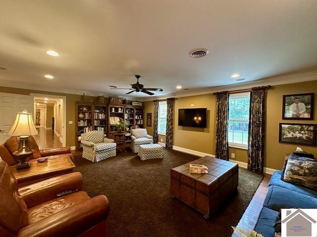 living room with visible vents, dark carpet, ornamental molding, a ceiling fan, and baseboards