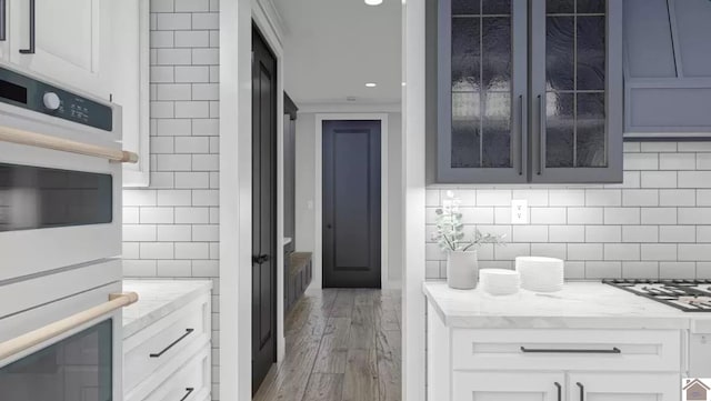 kitchen featuring white cabinets, stainless steel appliances, wood-type flooring, and backsplash