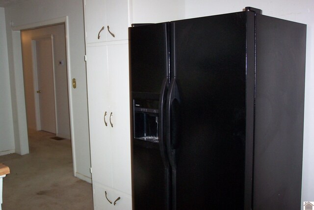 kitchen featuring black fridge, light carpet, and white cabinets