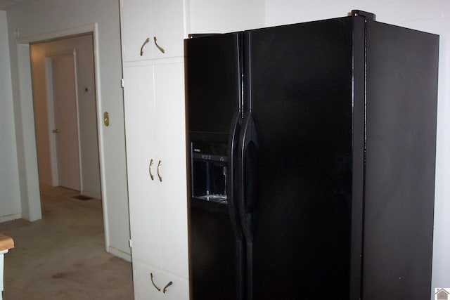 interior space with black fridge with ice dispenser and white cabinets