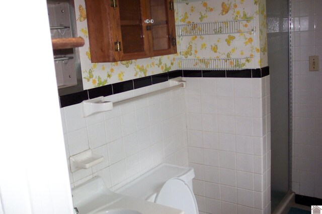 bathroom featuring an enclosed shower, tile walls, and toilet