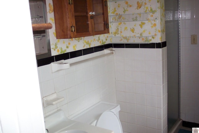 bathroom featuring toilet, an enclosed shower, and tile walls