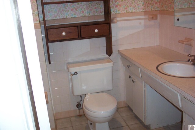 bathroom with tasteful backsplash, tile walls, tile patterned flooring, toilet, and vanity