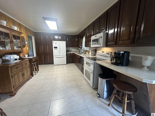 kitchen with dark brown cabinetry, light tile patterned floors, ornamental molding, a kitchen breakfast bar, and white appliances